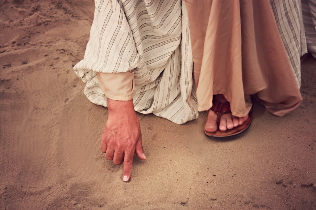 Close-up of a hand pointing on sand, wearing vintage clothing and sandals, emphasizing a cultural or historical theme.