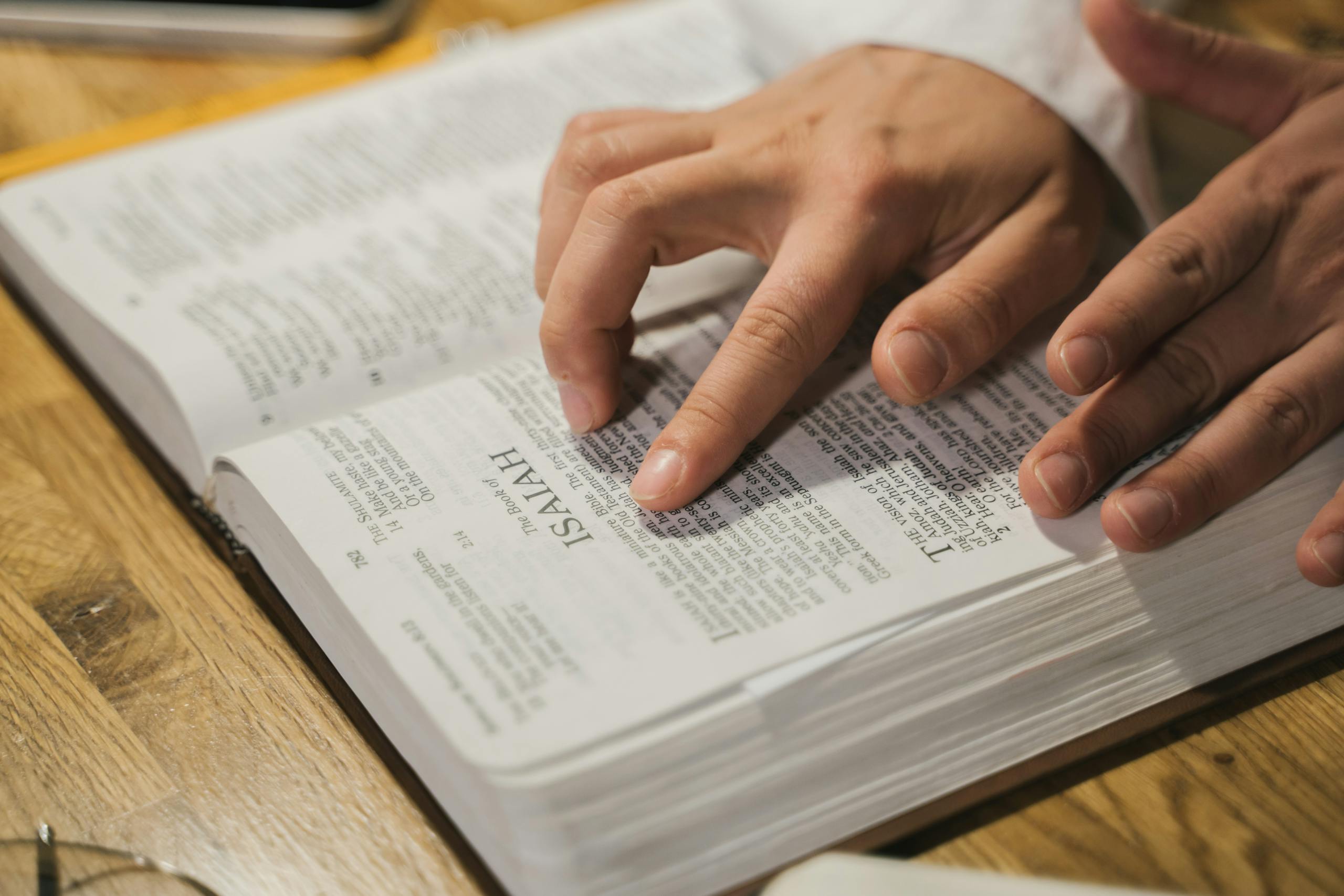 Close-up of hands reading a Bible, focusing on Isaiah passage, in an intimate indoor setting.